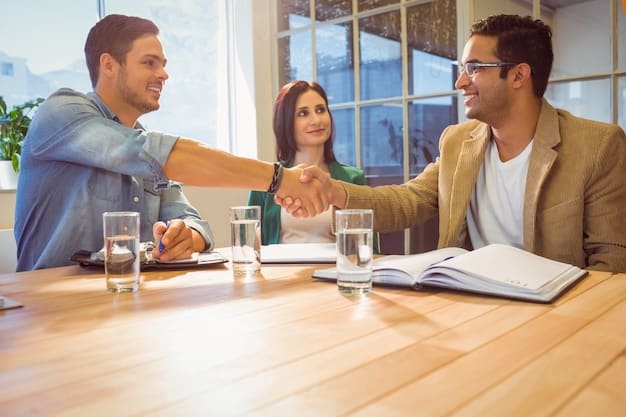 Two people sitting at a table, smiling and shaking hands over some documents. The scene suggests a successful negotiation or agreement.