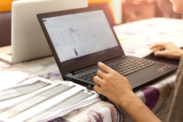 A close-up shot of a person's hands typing on a laptop, with a budgeting spreadsheet visible on the screen. The focus is on the details of the spreadsheet and the person's hands.